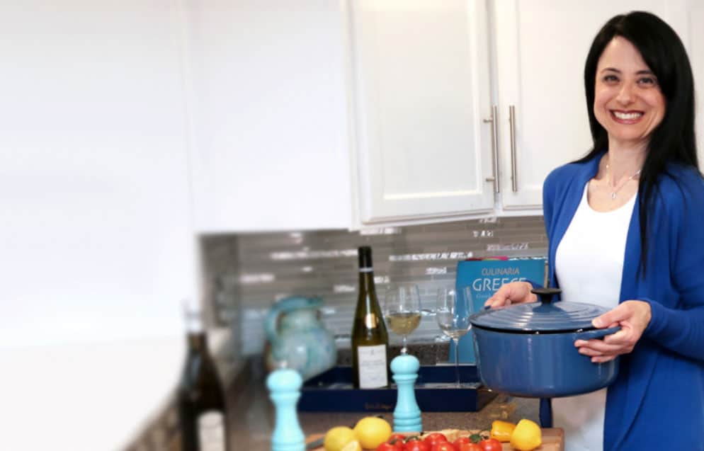 Voula Manousos, weight management and pregnancy nutritionist, stands in a white kitchen holding a blue pot with chopped vegetables on the counter