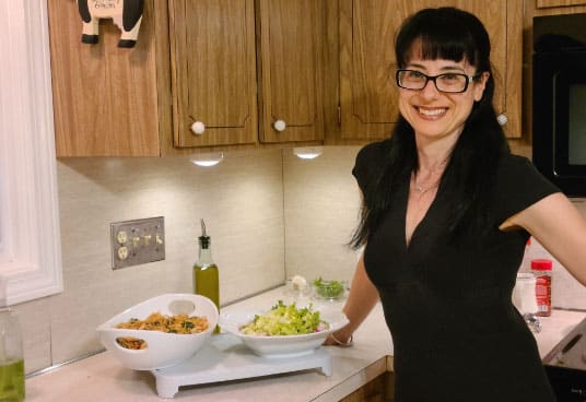 Voula Manousos, weight management nutrition dietitian, stands in a kitchen next to a prepared dish of pasta and salad