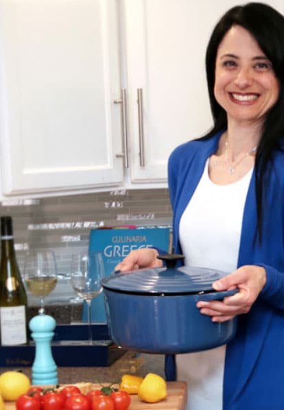 Voula Manousos, weight management and pregnancy nutritionist, stands in a white kitchen holding a blue pot with chopped vegetables on the counter next to her