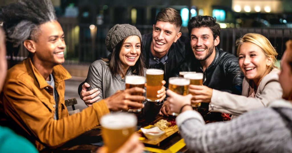 A group of young people clink beer glasses at a dinner