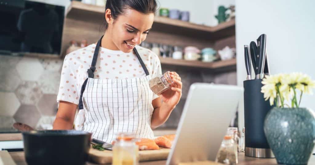 A woman holds up a spice above fresh salmon as she meal preps in the kitchen