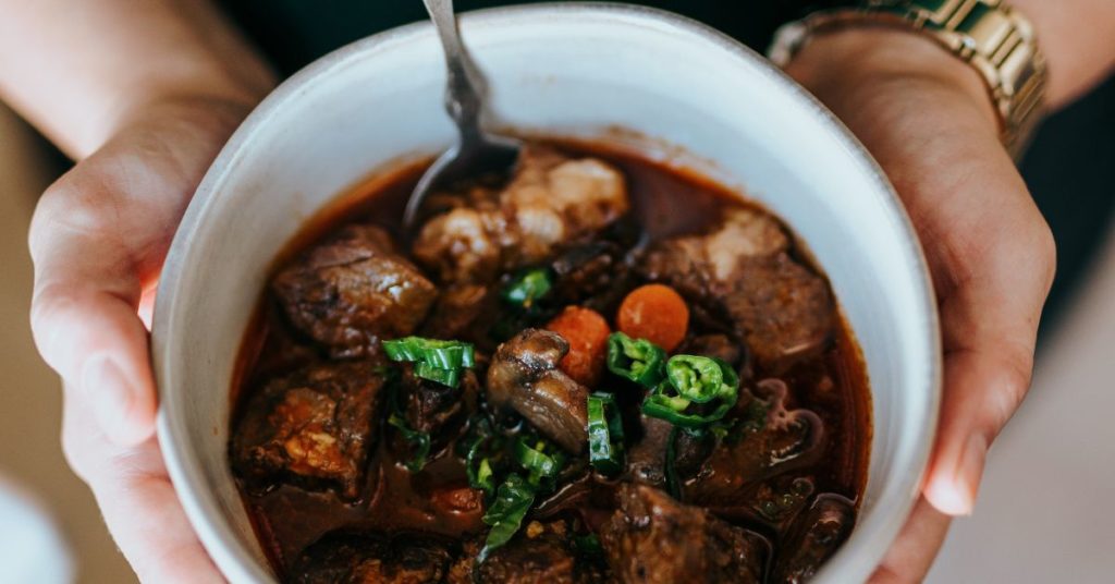 A woman's hand holds a bowl of beef stip stew