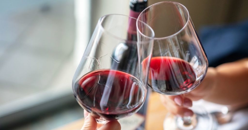 Two wine glasses filled with red wine clink in a toast | Alcohol and Weight Gain During Holidays