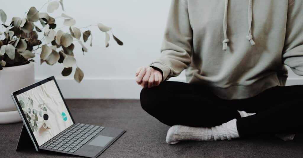 A person in comfortable clothing sits on their floor to meditate