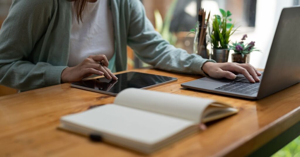 A woman researches on her laptop, tablet, and in a notebook to set her SMART weight loss goals