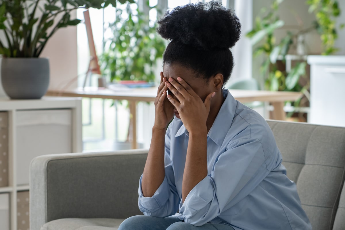 woman sitting on couch with head in her hands - fatigue sign of low protein in women (concept)