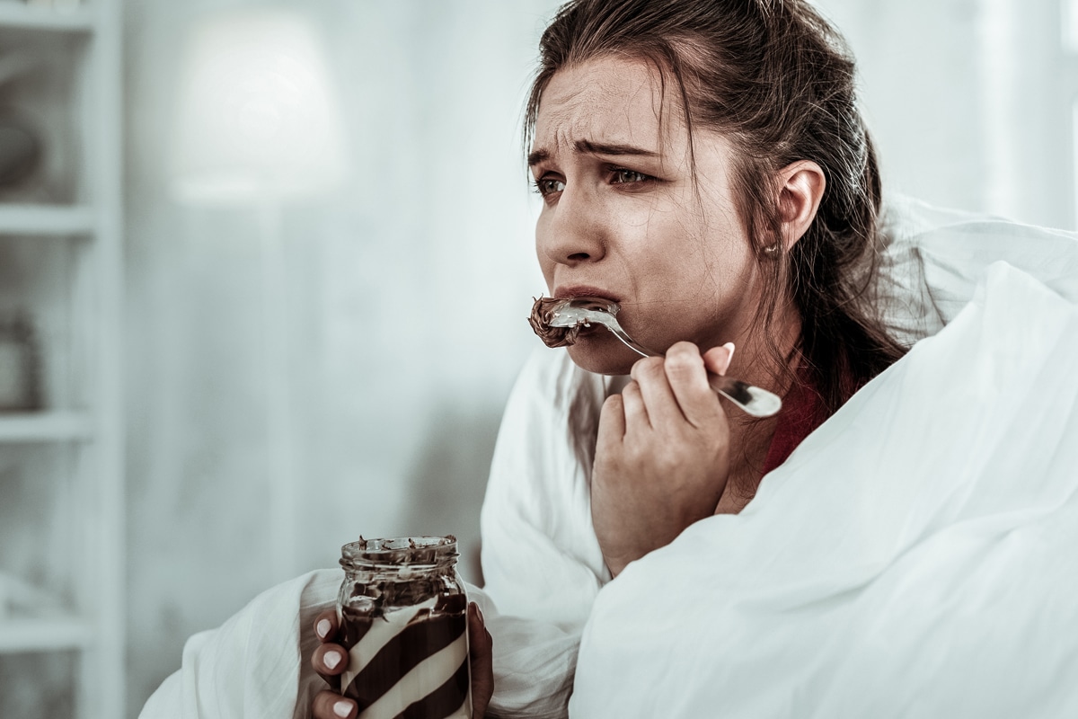 emotional eating triggers - woman on the couch eating ice cream and crying