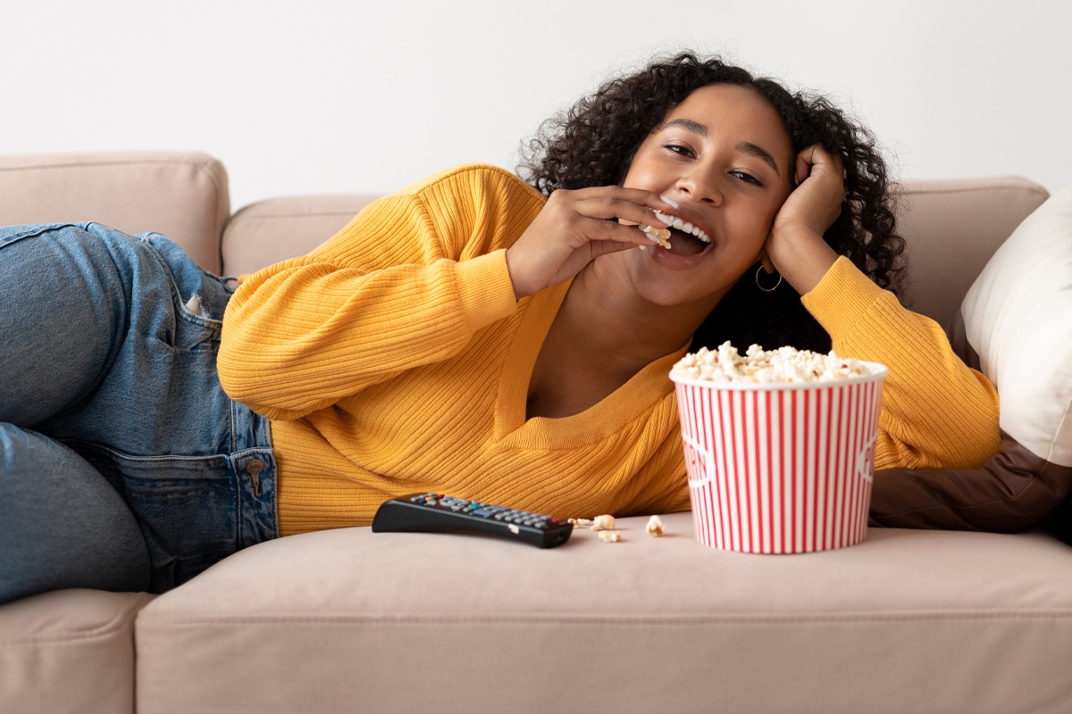 happy eating - woman eating popcorn on the couch out of habit instead of hunger