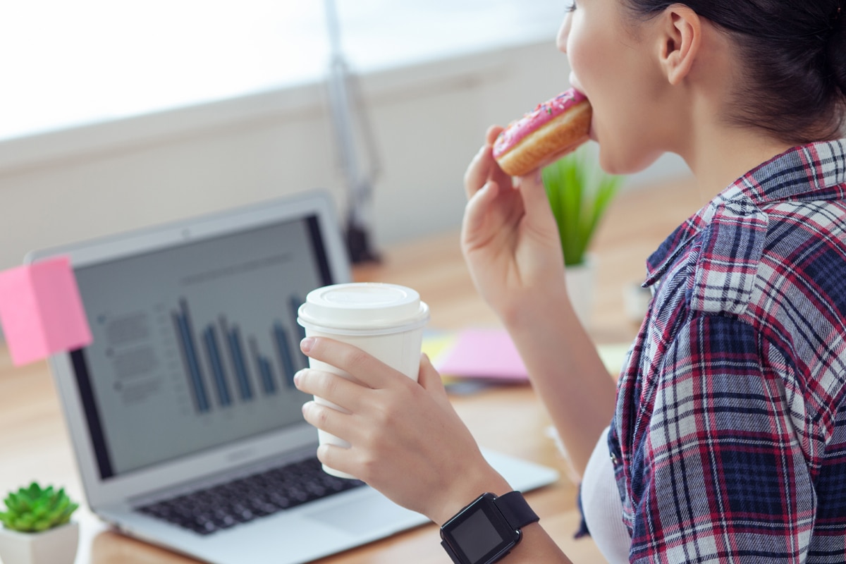 stress eating at work - woman at her desk eating a donut while looking at performance charts