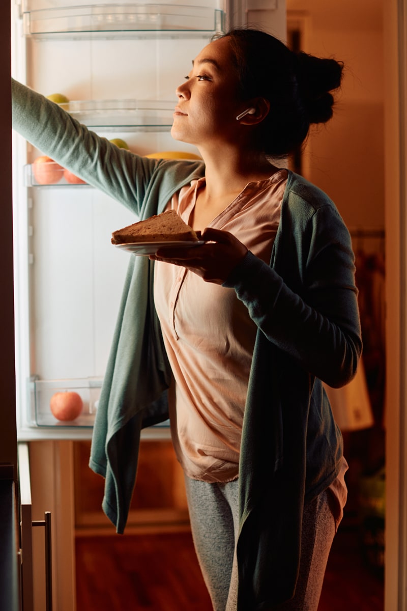 triggered eating - midnight snack - woman getting a snack from the fridge in her pajamas